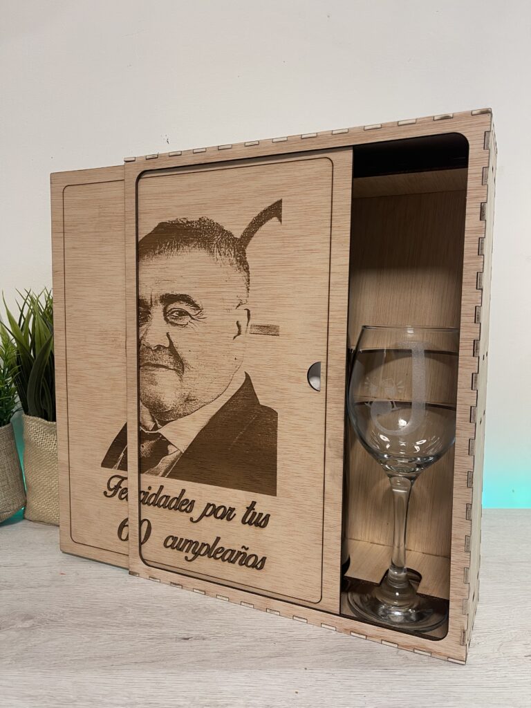 Caja de madera con tapa grabada con un retrato y un mensaje, junto a una copa