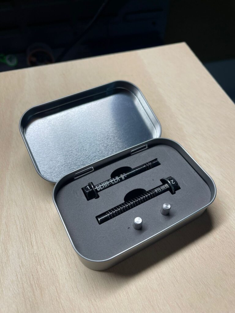 Estuche metálico abierto con dos piezas negras grabadas y dos piezas pequeñas plateadas